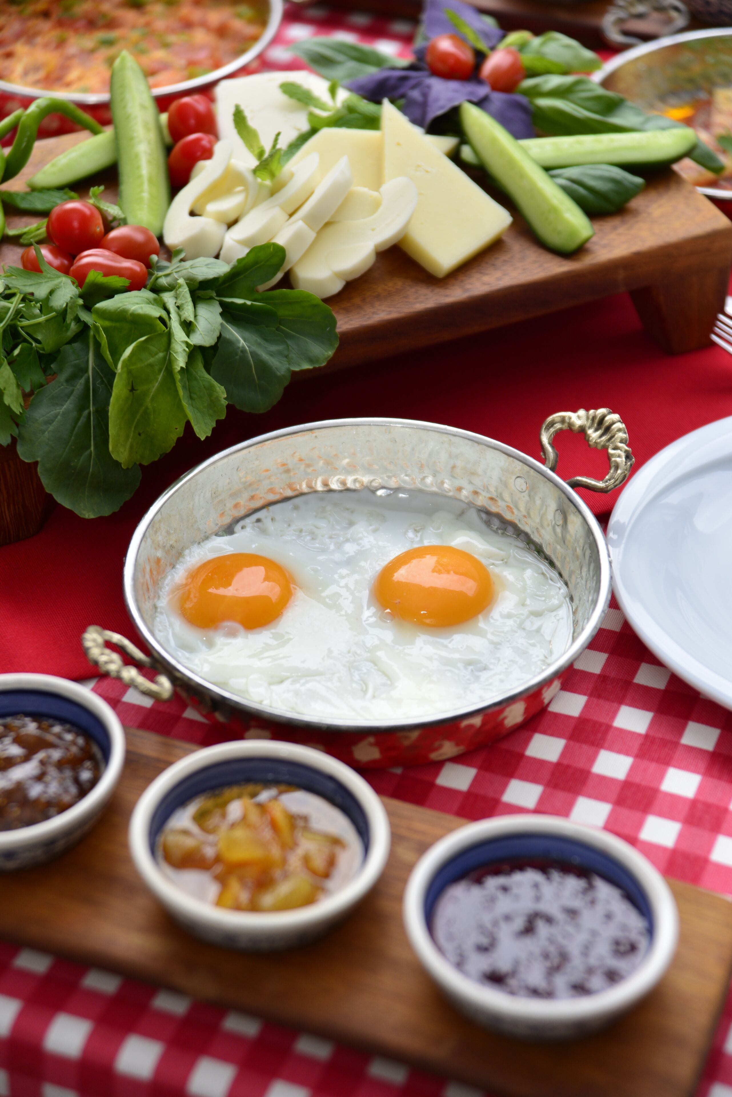 A breakfast setting with eggs, cheese, vegetables, and various condiments on a checkered tablecloth.