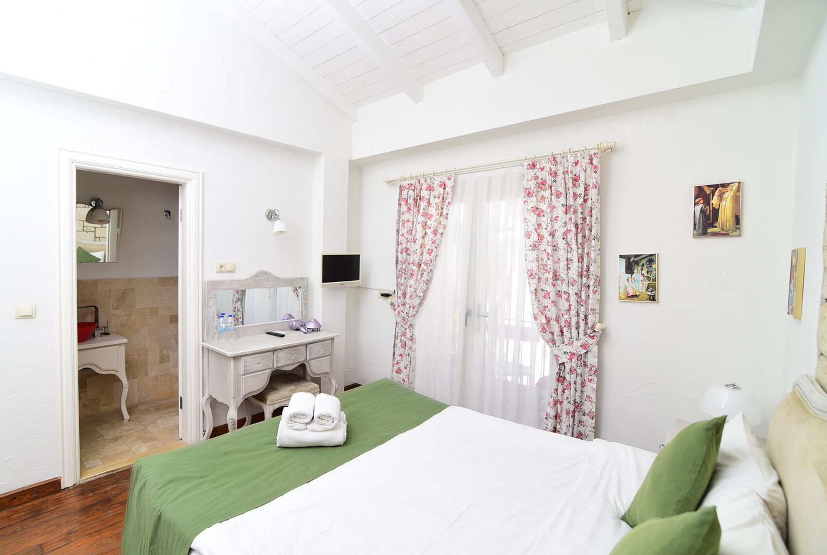 Habitación de hotel con cama, escritorio con espejo, televisor y baño visible a través de una puerta abierta.