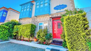 A building with a stone facade, blue shutters, and a red door. - Zübeyde Hanım Alaçatı (Cesme)