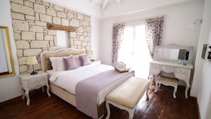 A bedroom with a stone wall, a bed with a bench, a dresser, and a mirror. - Zübeyde Hanım Alaçatı (Cesme)