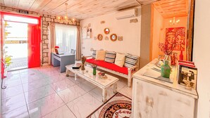 A spacious living area with a red sofa, a dining table, and a coffee table. There is a stone wall and a door labeled "EXIT". - Zübeyde Hanım Alaçatı (Cesme)