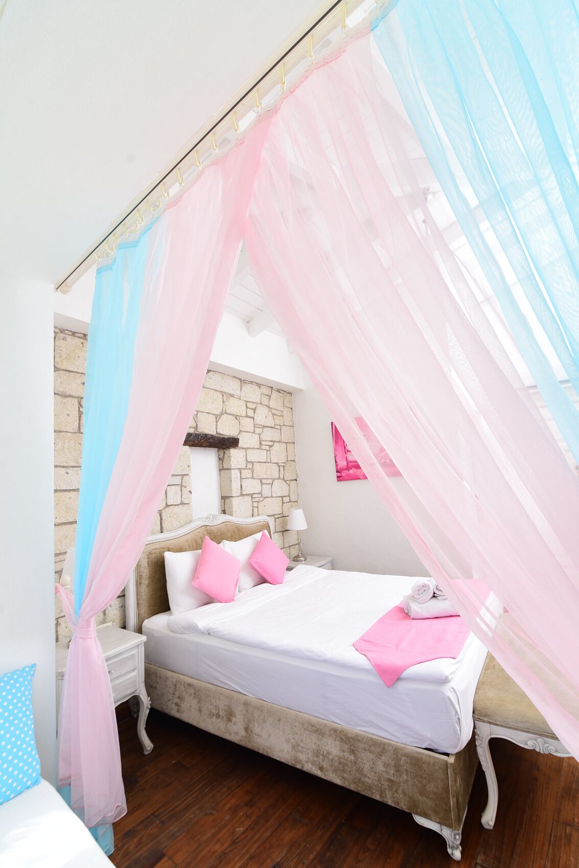 Une chambre à coucher avec un lit, une table de chevet, un mur en pierre et une fenêtre ornée de rideaux légers.