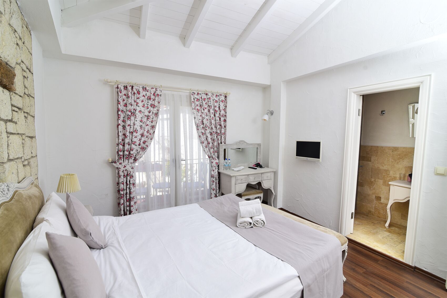 Camera d'albergo con un letto, una toeletta con specchio, una TV e un angolo doccia.