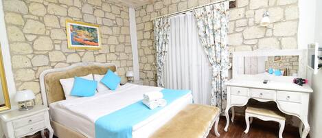 Un dormitorio con pared de piedra, una cama con ropa de cama azul, una mesita de noche con lámpara, un aparador y un banco.
