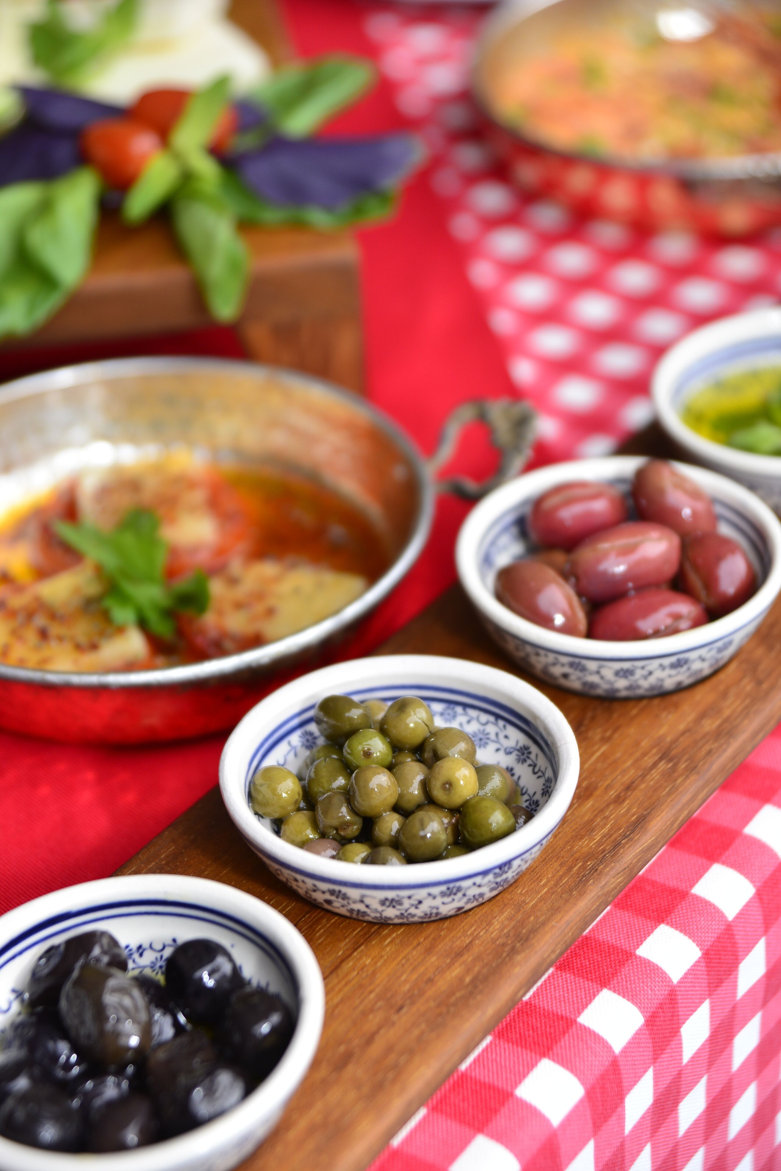 A wooden serving board with various bowls of olives and a bowl of soup.
