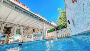 A swimming pool with a stone wall and a covered patio area. - Zübeyde Hanım Alaçatı (Cesme)