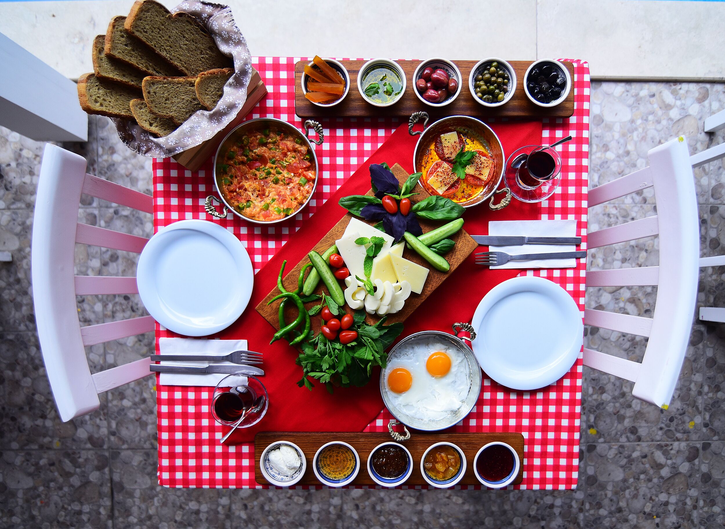 A table set with a variety of dishes, including bread, vegetables, cheese, and eggs, along with several small bowls of condiments.