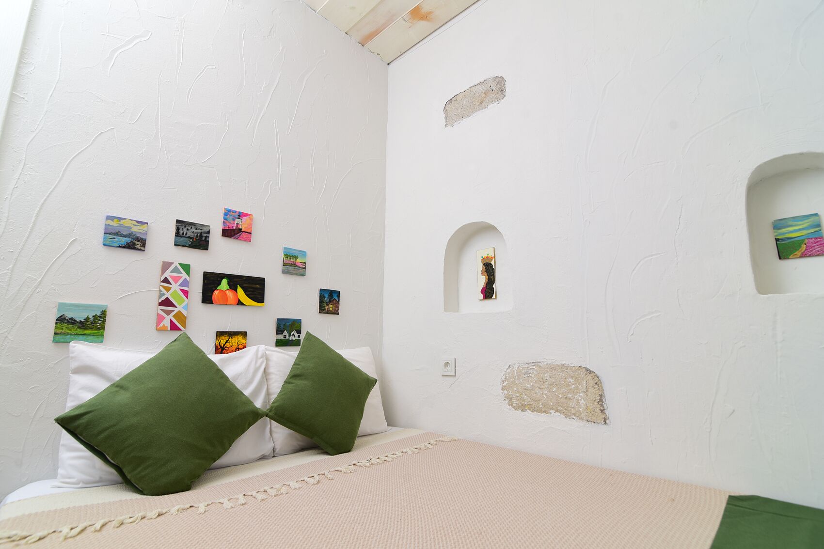 A bedroom with a bed, pillows, and a wall decorated with various small paintings.