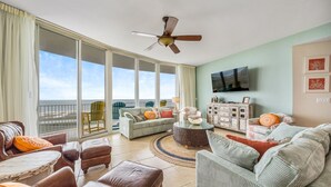 A spacious living room with a large window, a ceiling fan, and a flat-screen TV mounted on the wall.
