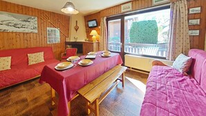 A cozy room with wooden walls, a red sofa, a wooden bench, and a dining table set for two. - Cozy 2-room apartment, 6 beds, near slopes (Le Grand-Bornand)