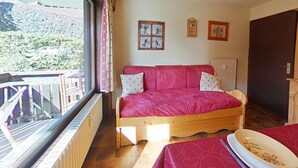 A cozy room with a wooden bed, a window with a view of greenery, and a small table with a bowl. - Cozy 2-room apartment, 6 beds, near slopes (Le Grand-Bornand)