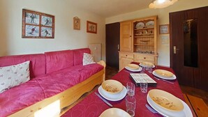 A cozy room with a red sofa, wooden dining table set with plates and glasses, and a cabinet with dishes. - Cozy 2-room apartment, 6 beds, near slopes (Le Grand-Bornand)