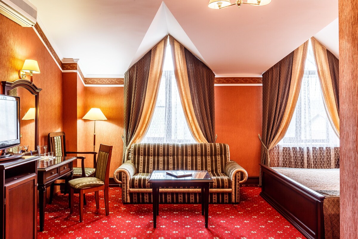 A hotel room with a sofa, a small table, a TV, and a desk with a chair.