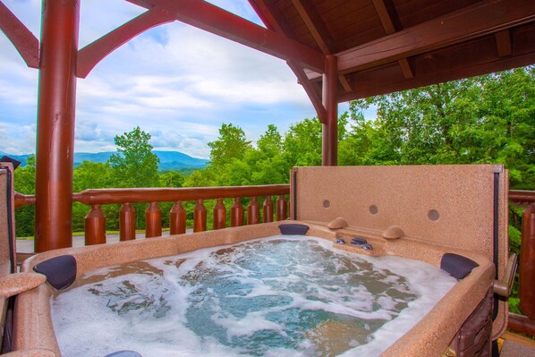 Ein Whirlpool mit einer Holzterrasse und Blick auf grüne Bäume und Berge.