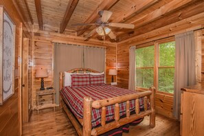 Ein Schlafzimmer einer Holzhütte mit einem Bett, einem Deckenventilator und großen Fenstern.