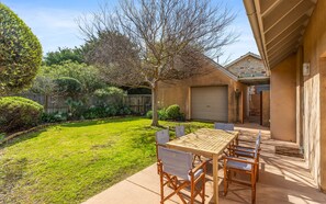 A backyard with a wooden table and chairs, surrounded by a well-maintained lawn and a wooden fence.