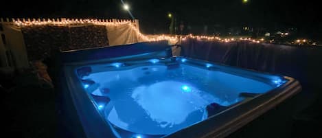 An outdoor hot tub with a stone wall and string lights.