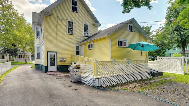 A two-story yellow house with a porch, a white fence, and a blue hose.