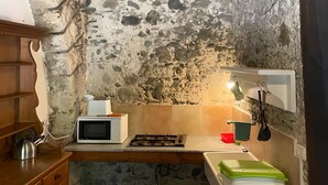 A rustic kitchen with a stone wall, wooden ceiling beams, a microwave, a gas stove, and a kettle. - Casa Felice Uno - Contrada Guido (con piscina) (Sellia Marina)
