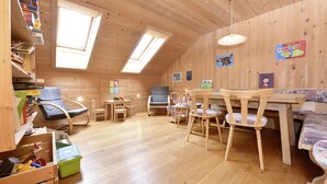 Een gezellige, goed verlichte kamer met houten wanden en een schuine kap, met een eethoek met stoelen, een tafel en kinderspeelgoed.