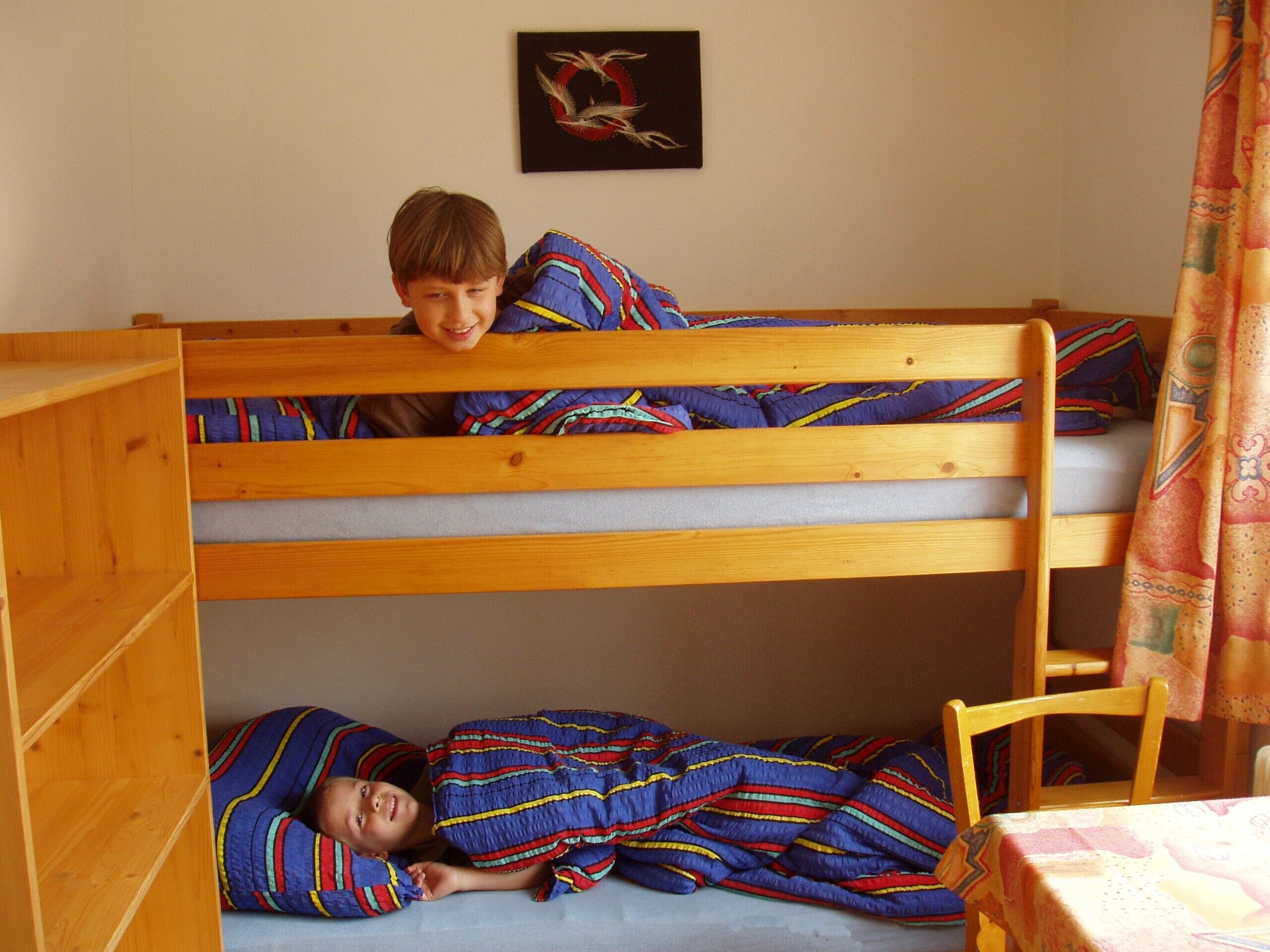 A bunk bed room with two children sleeping, a wooden table, and a wall decoration.
