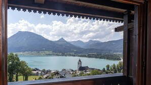 A view from a wooden balcony with a decorative railing, overlooking a lake with mountains in the background and a church with a tower. - Altroiterhof (Sankt Wolfgang im Salzkammergut)
