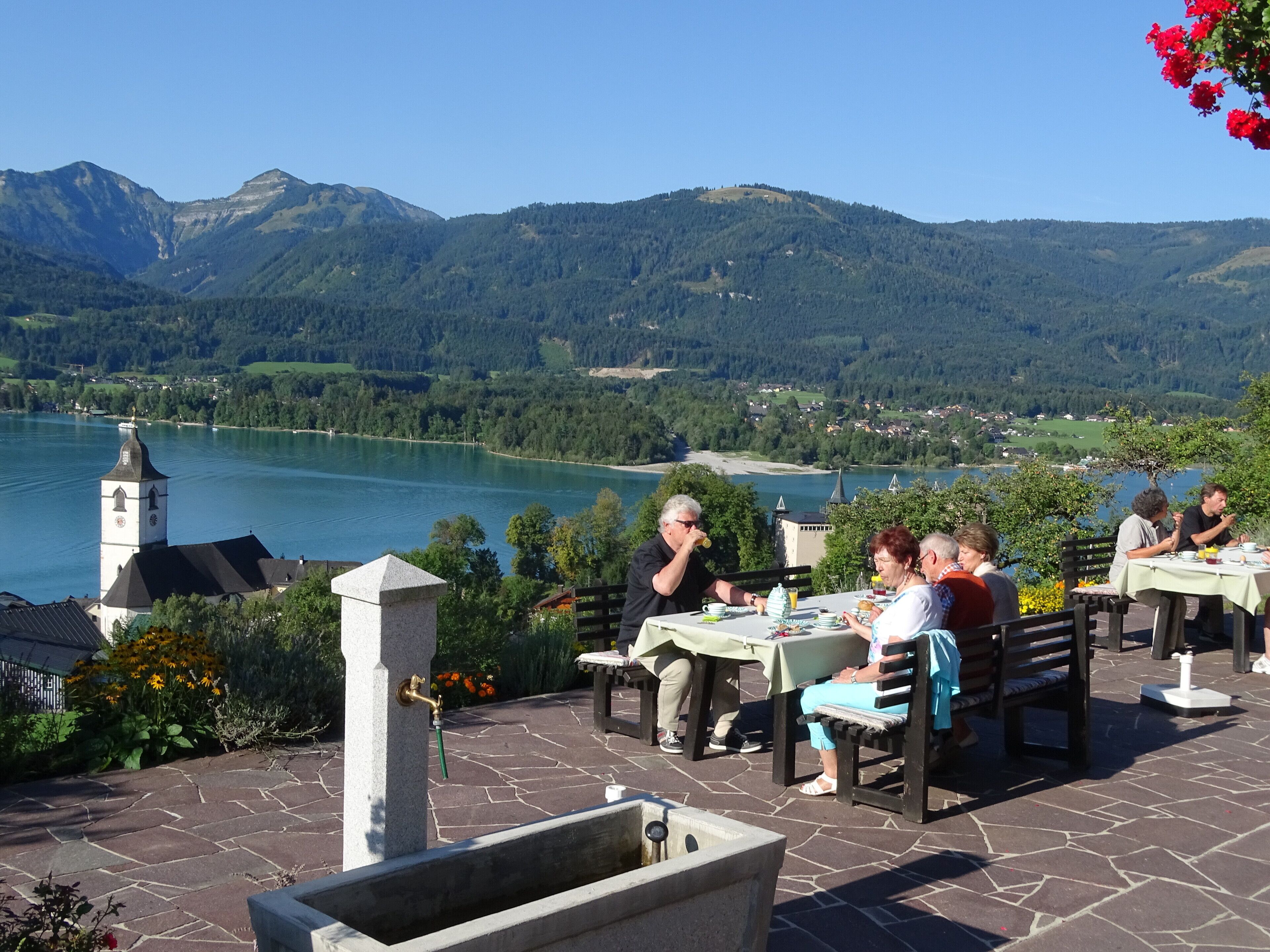 Un espace extérieur aménagé pour les repas, avec des tables et des chaises, offrant une vue sur un lac et des montagnes.