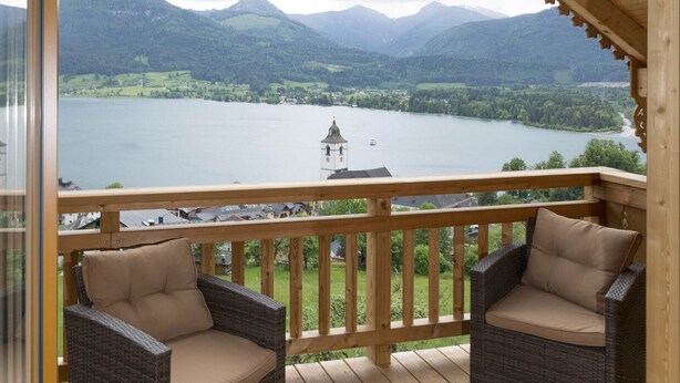 A balcony with wicker chairs and a wooden railing overlooking a lake and mountains. - Altroiterhof (Sankt Wolfgang im Salzkammergut)