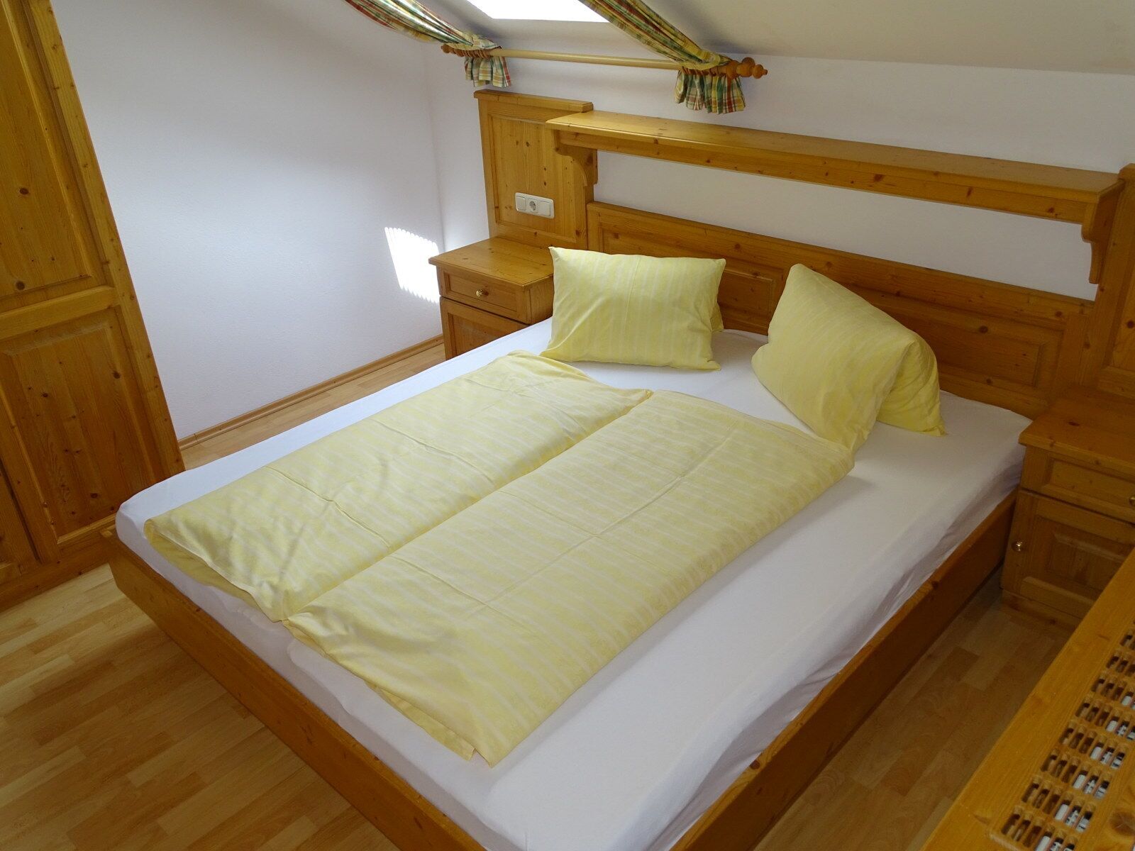 A wooden bed with a headboard, two bedside tables, and a window with curtains.