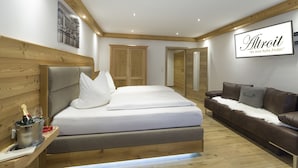 A modern hotel room with a large bed, a wooden headboard, a brown leather sofa, and a wooden wardrobe. - Altroiterhof (Sankt Wolfgang im Salzkammergut)