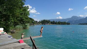 Eine Holzstege, der sich in einen See mit klarem Wasser erstreckt, umgeben von üppiger Vegetation und Bergen im Hintergrund.