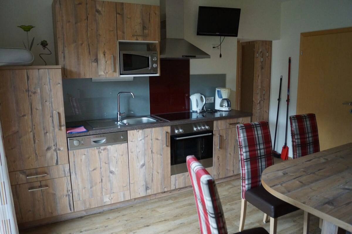 Keittiössä on puiset kaapit, mikroaaltouuni, liesi, pesuallas ja ruokailutila, jossa on ruutukuosiset tuolit.