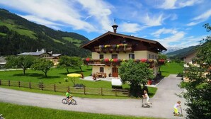 A traditional chalet with a balcony adorned with flowers, a paved driveway, and a surrounding green landscape. - Reiterhof (Sankt Johann im Pongau)