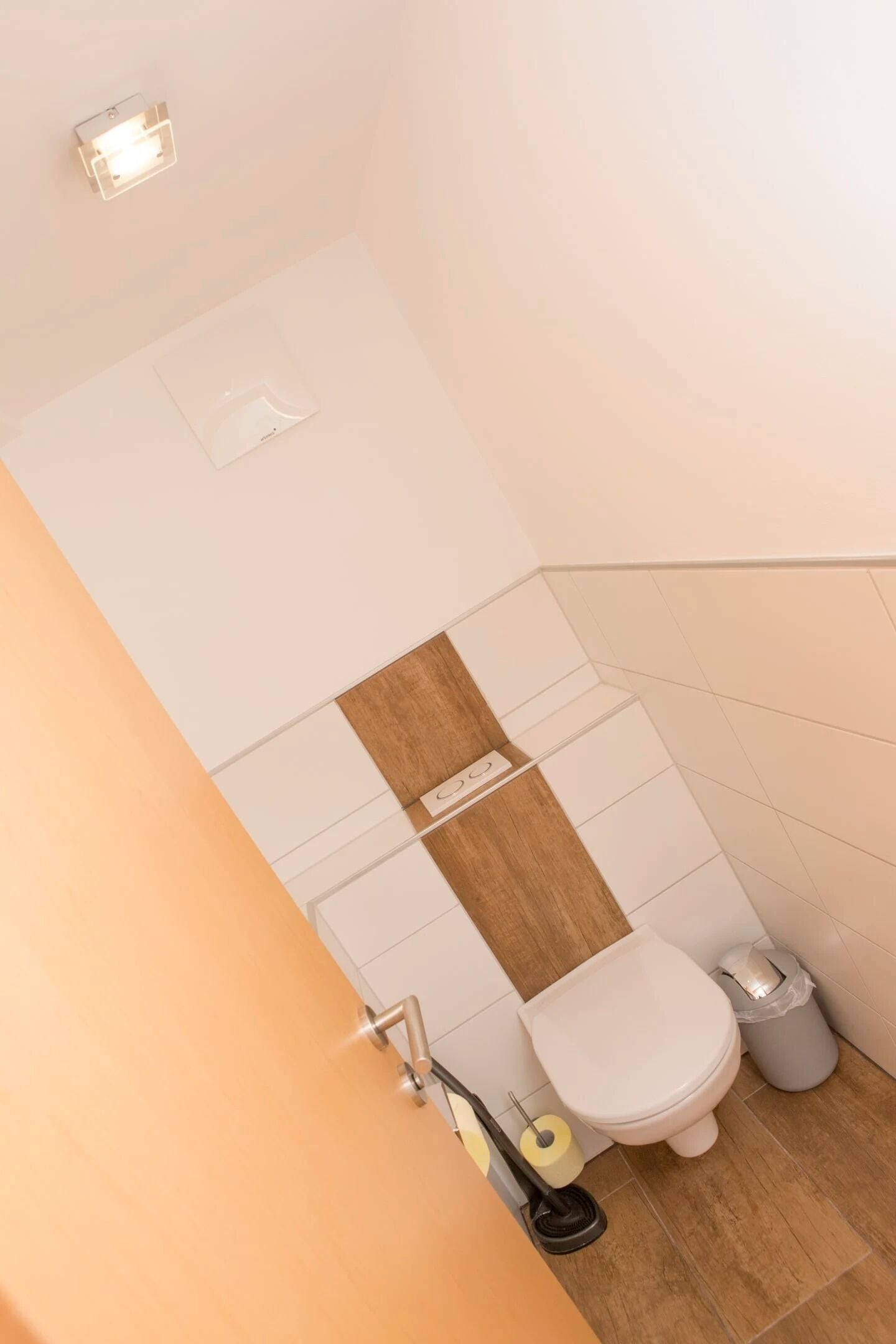 A small bathroom with a toilet, a trash bin, and a toilet paper holder.