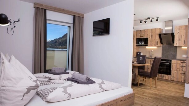 A bedroom with a large bed, a view of the mountains, and a kitchenette with wooden cabinets. - Reiterhof (Sankt Johann im Pongau)