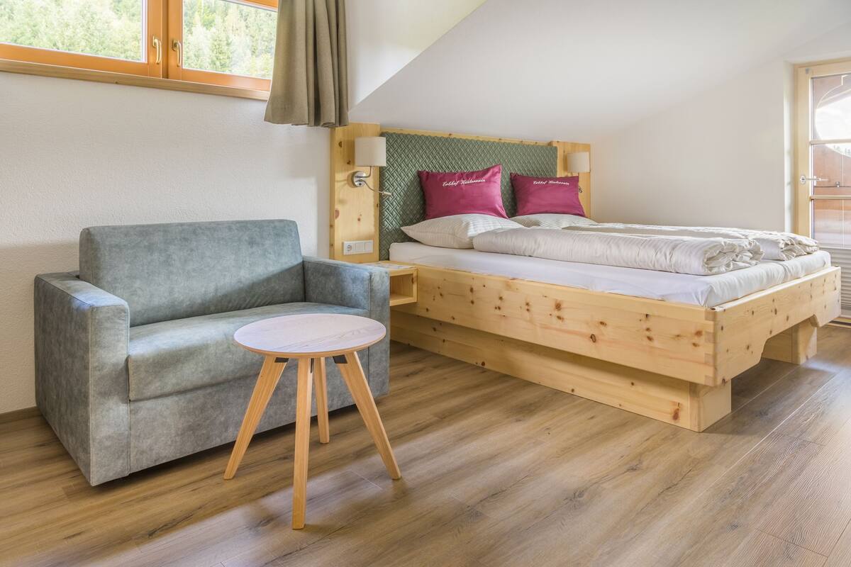 A loft-style bedroom with a wooden bed, grey sofa, and a small round table.