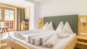 A neatly made bed with white linens, a wooden headboard, and a view of a balcony with a chair and table. - Erbhof Hinterrain (Leogang)
