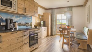 A modern kitchen with wooden cabinets, a built-in oven, and a coffee maker. There is a dining area with a table and chairs, and a window with a view of the outdoors. - Erbhof Hinterrain (Leogang)