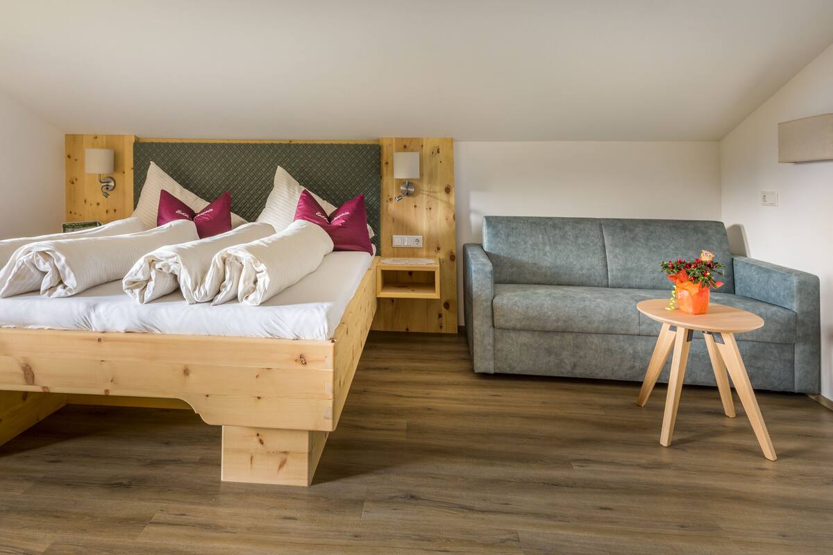 A room with a wooden bed, a grey sofa, and a small table with a vase.