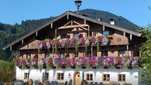 A traditional wooden chalet with balconies adorned with colorful flowers, set against a mountainous backdrop. - Erbhof Hinterrain (Leogang)