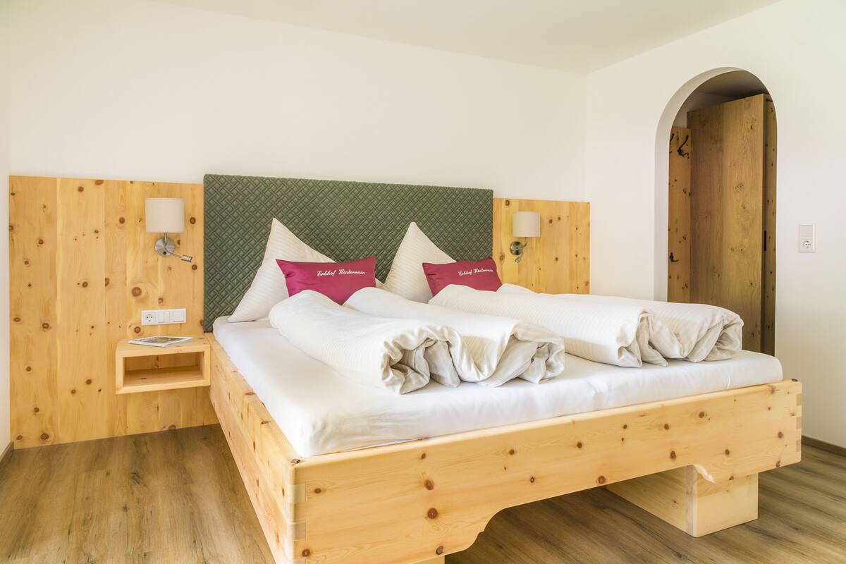 A wooden bed with a green headboard, two pillows, a nightstand, and a wall-mounted lamp.