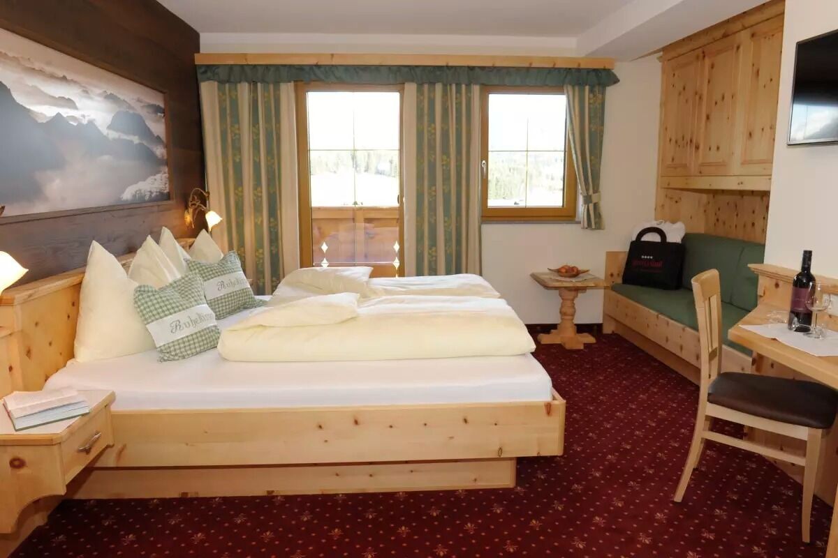 A wooden bed with pillows, a small table with a bottle, a chair, and a couch.