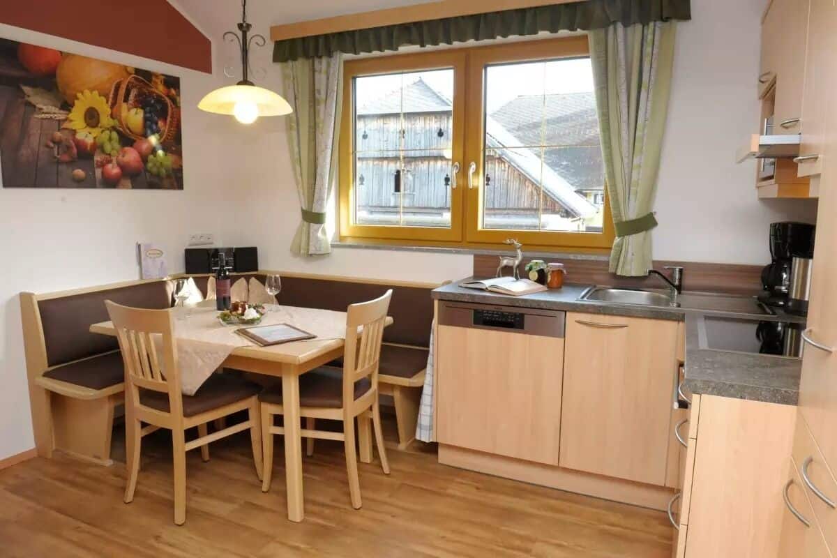 A cozy kitchen with wooden cabinets, a dining table with chairs, a window with curtains, and a painting on the wall.