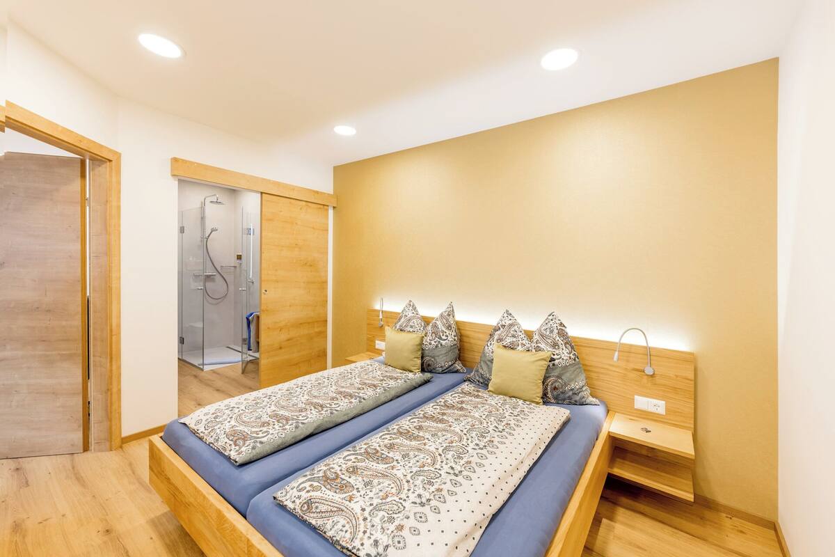 Un dormitorio moderno con una cama grande, cabecera de madera y ducha a pie.