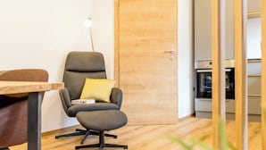 A modern room with a wooden floor, a grey armchair with a yellow pillow, a wooden door with a cross, and a small table.