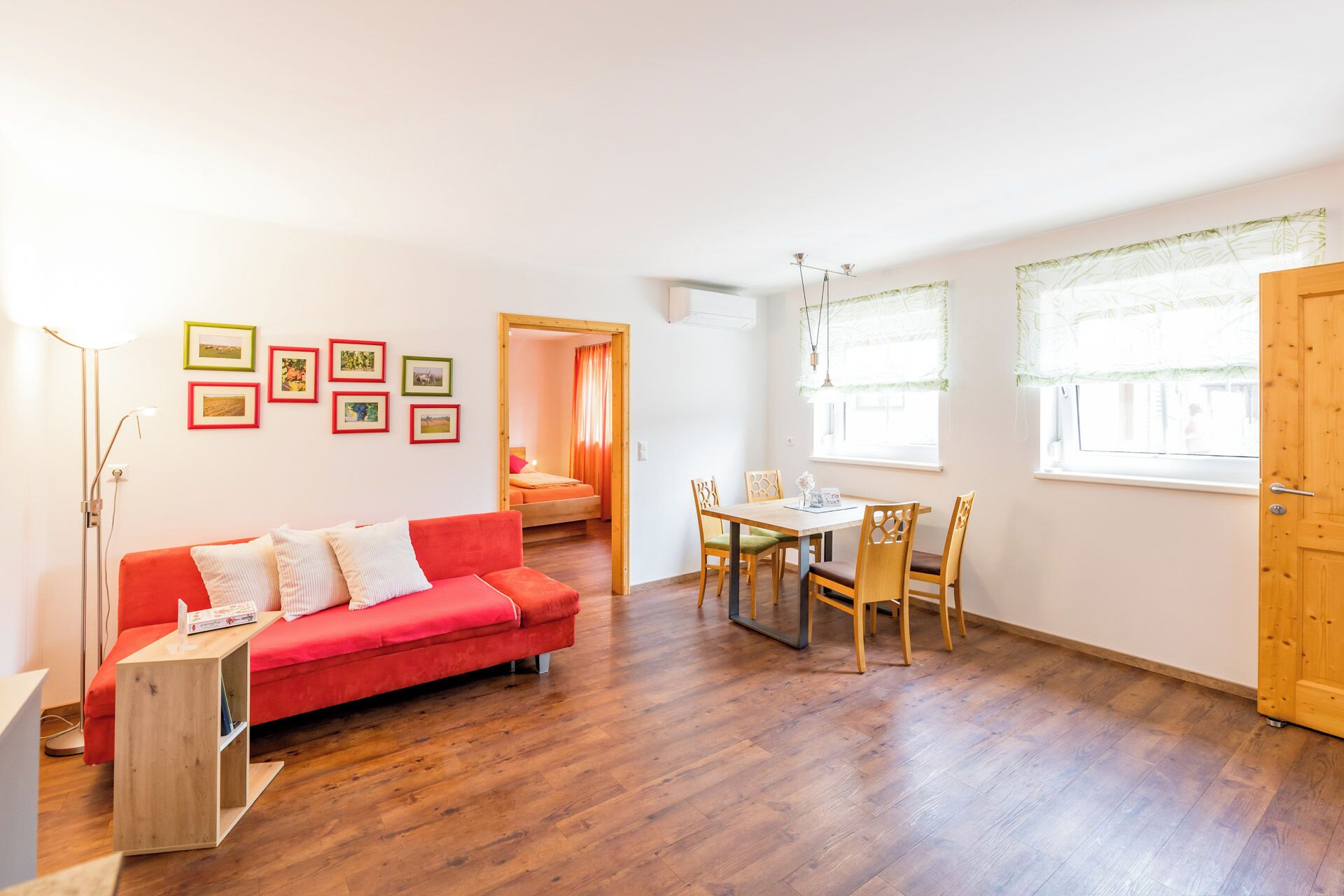 Uma sala de estar luminosa com um sofá vermelho, uma mesa de jantar de madeira e uma porta de madeira.