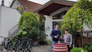 A courtyard with bicycles, a wine barrel, and a house with a sloped roof. - Familie Bauer – Bioweingut Bauer (Großriedenthal)