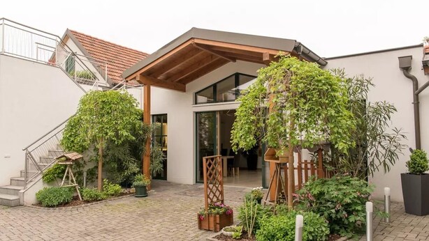 A modern house with a covered porch, a staircase, and a garden with various plants. - Familie Bauer – Bioweingut Bauer (Großriedenthal)