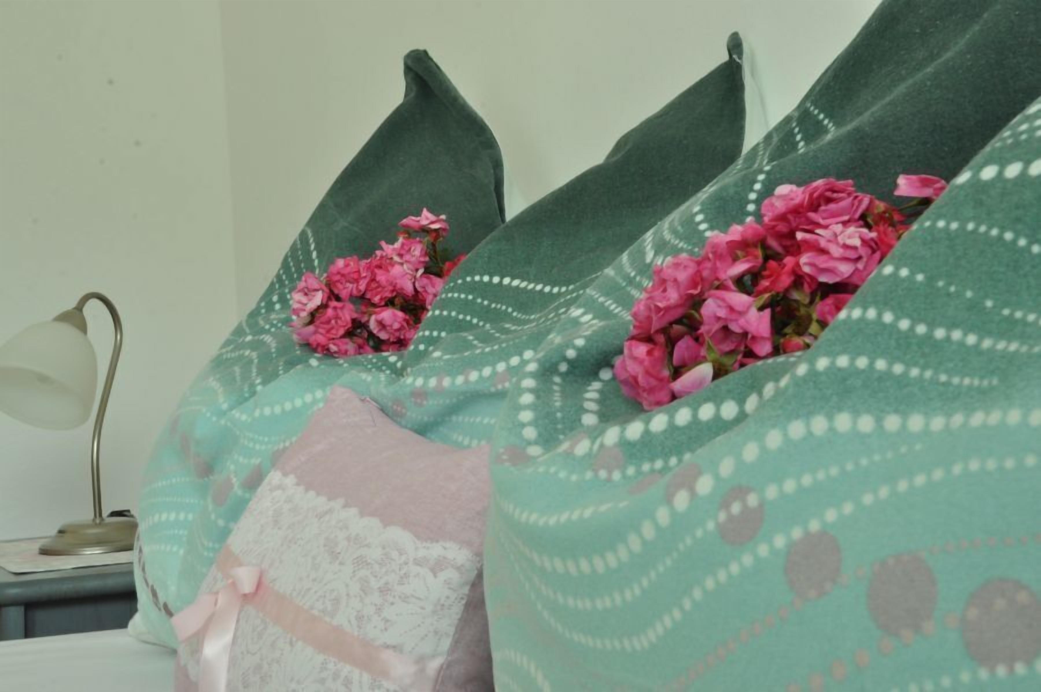 A bed with pillows featuring a green and white pattern, and pink flowers.