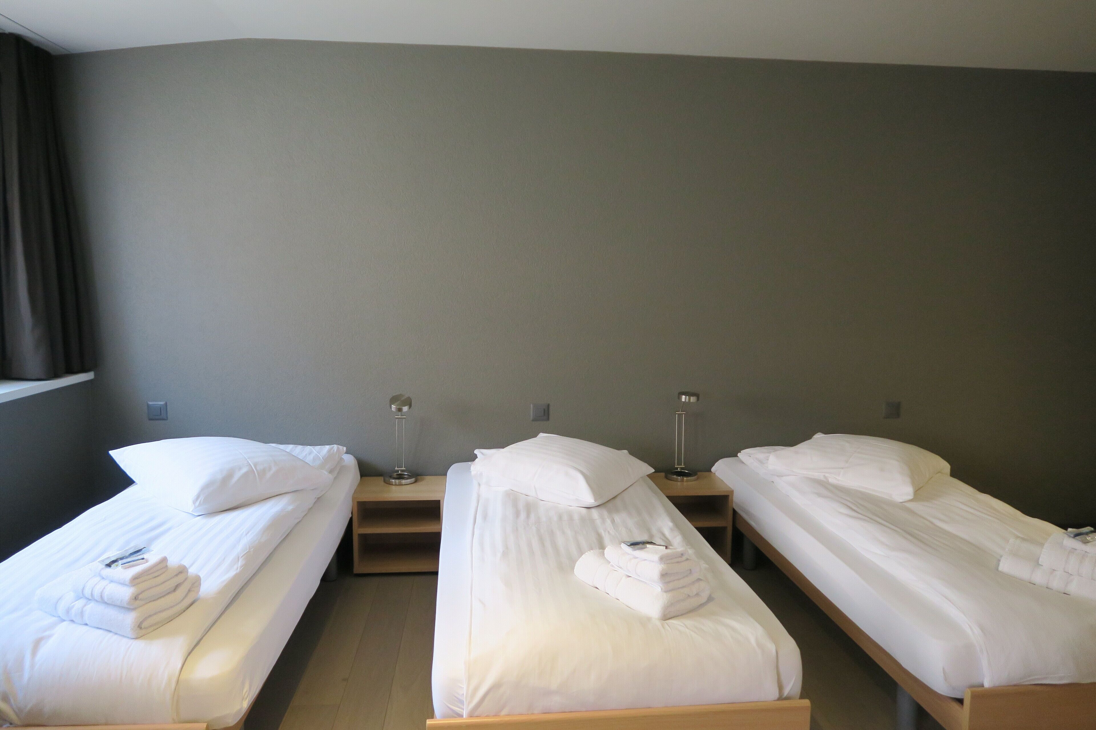 Une chambre d’hôtel avec deux lits simples, chacun comprenant un oreiller, une serviette roulée et une table de chevet avec une lampe.